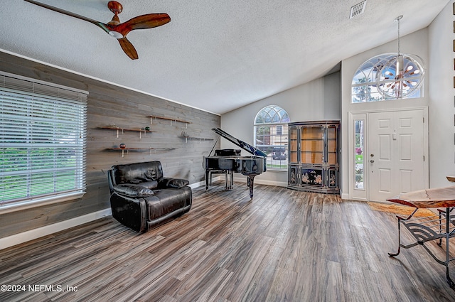 foyer with a textured ceiling, wood walls, wood-type flooring, ceiling fan, and vaulted ceiling