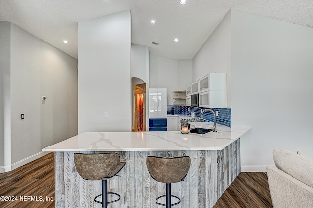 kitchen with a textured ceiling, dark hardwood / wood-style floors, a kitchen breakfast bar, kitchen peninsula, and light stone counters