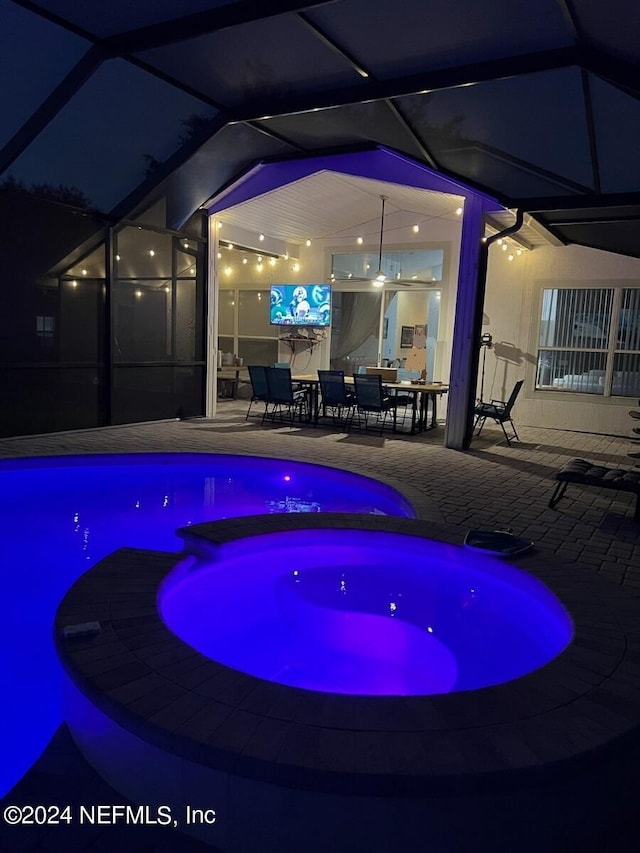 pool at night featuring a lanai, a patio area, and an in ground hot tub