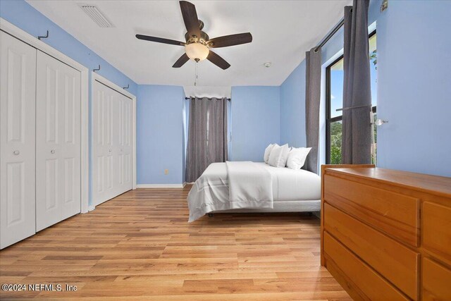 bedroom featuring light wood-type flooring, two closets, and ceiling fan