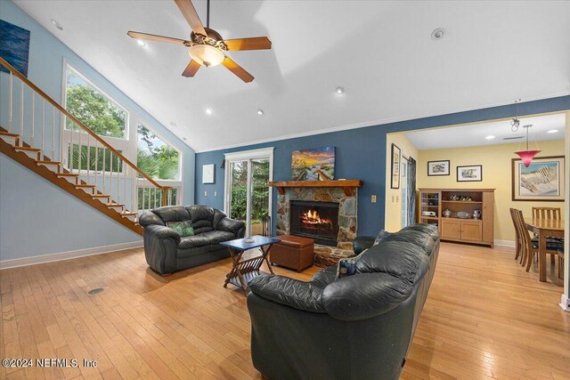 living room featuring high vaulted ceiling, a stone fireplace, ceiling fan, and light hardwood / wood-style floors