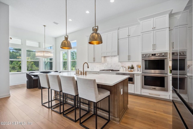 kitchen with pendant lighting, white cabinetry, light hardwood / wood-style flooring, and stainless steel appliances