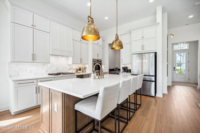 kitchen featuring pendant lighting, appliances with stainless steel finishes, an island with sink, white cabinetry, and light wood-type flooring