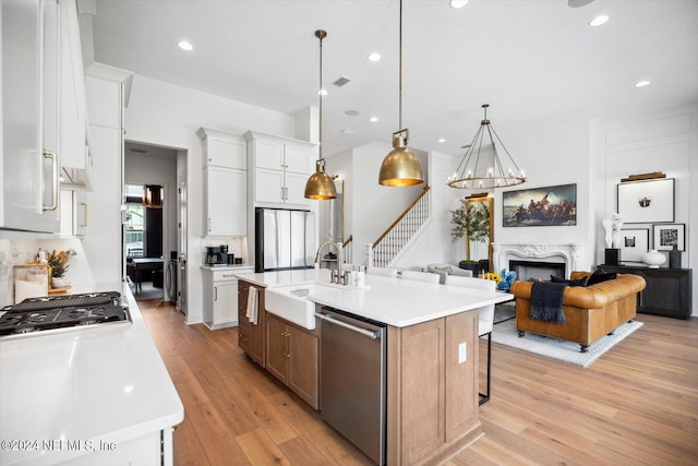 kitchen with appliances with stainless steel finishes, white cabinetry, sink, a premium fireplace, and a center island with sink