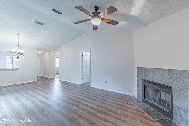 unfurnished living room with a healthy amount of sunlight, ceiling fan with notable chandelier, a tile fireplace, and dark wood-type flooring