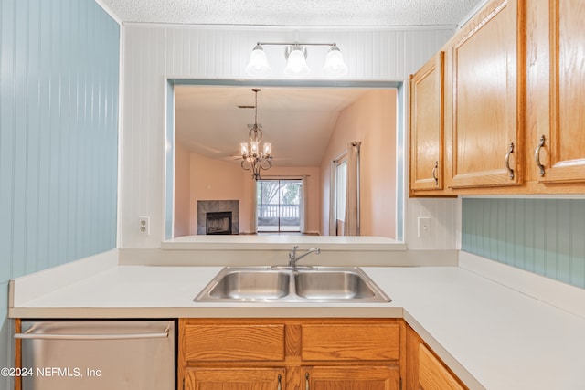 kitchen with a textured ceiling, stainless steel dishwasher, sink, and a notable chandelier