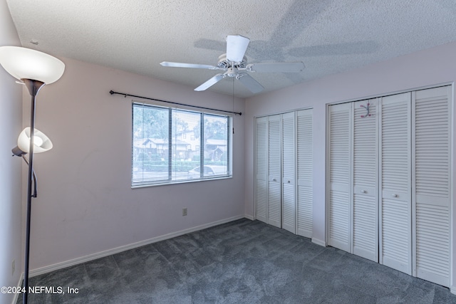 unfurnished bedroom with ceiling fan, dark colored carpet, a textured ceiling, and multiple closets