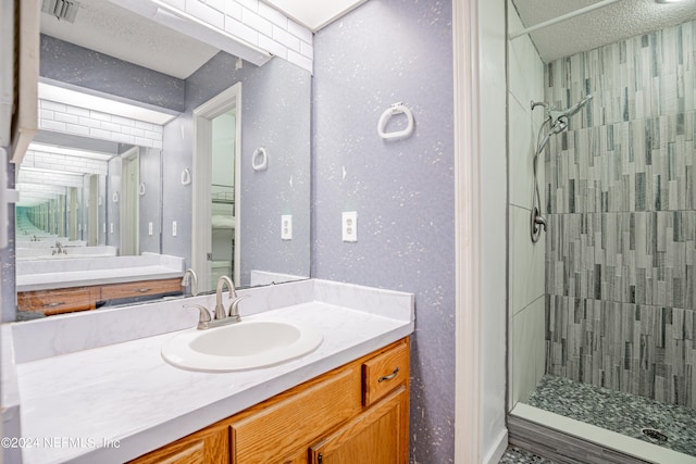 bathroom with tiled shower, vanity, and a textured ceiling