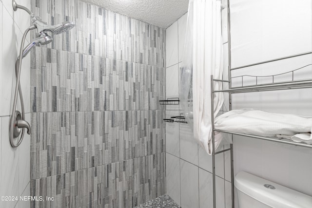 bathroom featuring toilet, tiled shower, and a textured ceiling