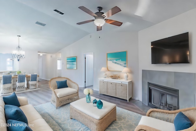 living room featuring hardwood / wood-style floors, ceiling fan with notable chandelier, a tile fireplace, and vaulted ceiling