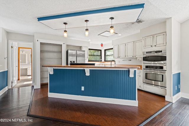 kitchen featuring appliances with stainless steel finishes, a textured ceiling, decorative light fixtures, and dark hardwood / wood-style floors