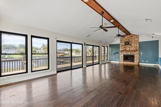 unfurnished living room featuring lofted ceiling with beams, a stone fireplace, a water view, hardwood / wood-style flooring, and a textured ceiling