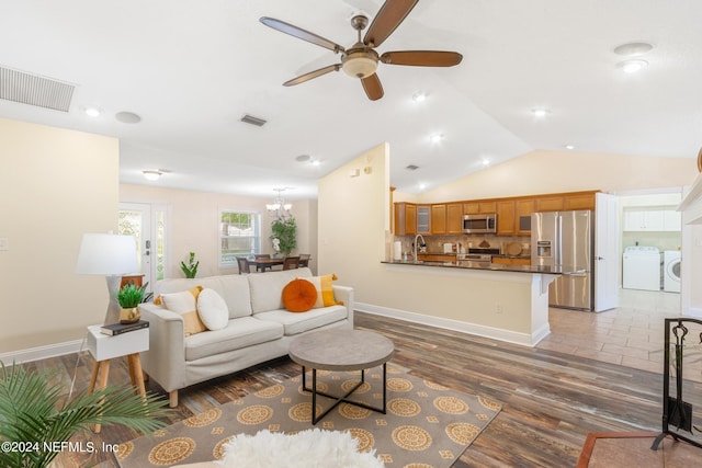 living room featuring light wood-type flooring, ceiling fan with notable chandelier, washer and clothes dryer, and vaulted ceiling