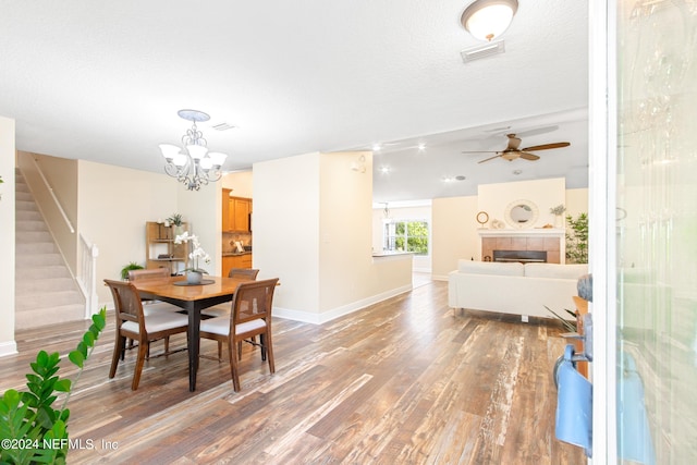 dining room with a tiled fireplace, ceiling fan with notable chandelier, hardwood / wood-style floors, and a textured ceiling