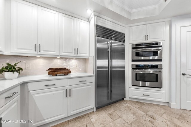 kitchen featuring backsplash, white cabinets, a raised ceiling, crown molding, and appliances with stainless steel finishes