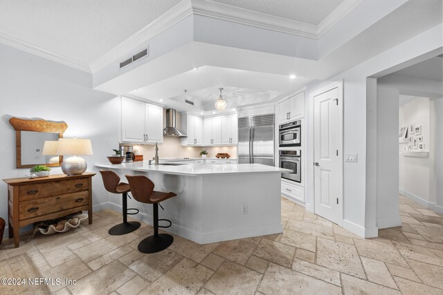 kitchen featuring kitchen peninsula, appliances with stainless steel finishes, white cabinetry, and wall chimney range hood