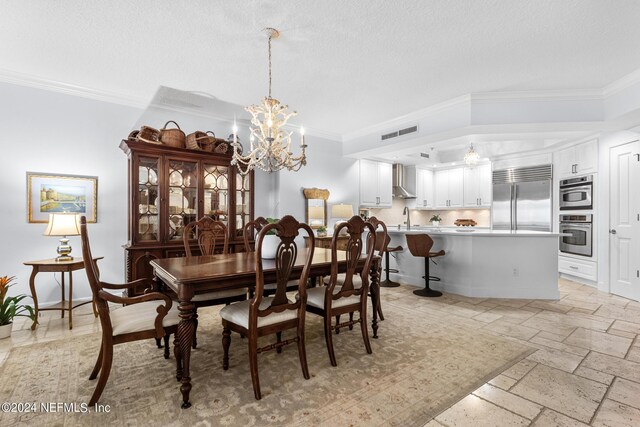 dining area featuring crown molding, sink, a textured ceiling, and an inviting chandelier