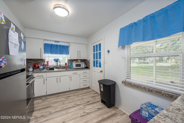 kitchen featuring white cabinets, light hardwood / wood-style flooring, backsplash, range, and stainless steel refrigerator