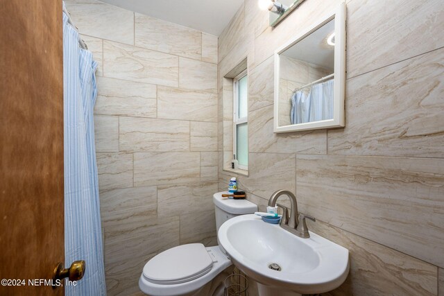 bathroom featuring tile walls, a shower with curtain, sink, and toilet