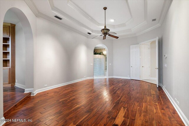 unfurnished room featuring a tray ceiling, dark wood-type flooring, ornamental molding, and ceiling fan