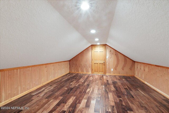 additional living space featuring lofted ceiling, dark hardwood / wood-style floors, a textured ceiling, and wood walls