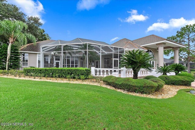 back of house with glass enclosure and a lawn