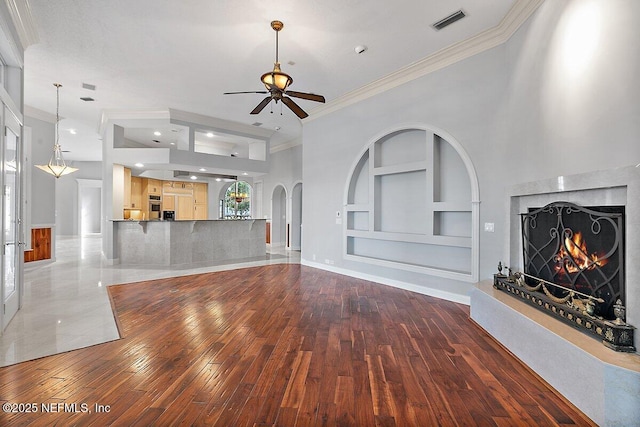 unfurnished living room with built in shelves, ornamental molding, ceiling fan, a premium fireplace, and hardwood / wood-style floors