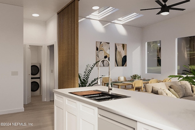 kitchen featuring light hardwood / wood-style flooring, stacked washer / drying machine, sink, white cabinetry, and ceiling fan