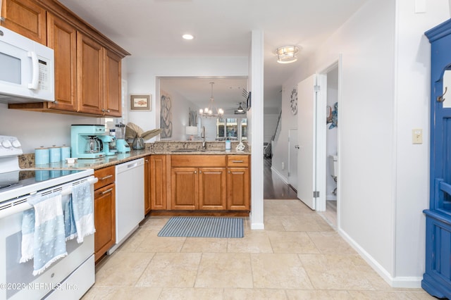 kitchen with white appliances, a chandelier, light stone counters, sink, and kitchen peninsula