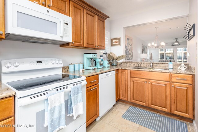 kitchen with ceiling fan with notable chandelier, white appliances, kitchen peninsula, sink, and light stone countertops