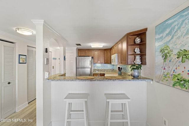 kitchen featuring ornamental molding, tasteful backsplash, light stone counters, kitchen peninsula, and stainless steel refrigerator