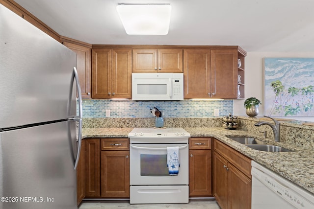 kitchen with backsplash, light stone counters, white appliances, and sink