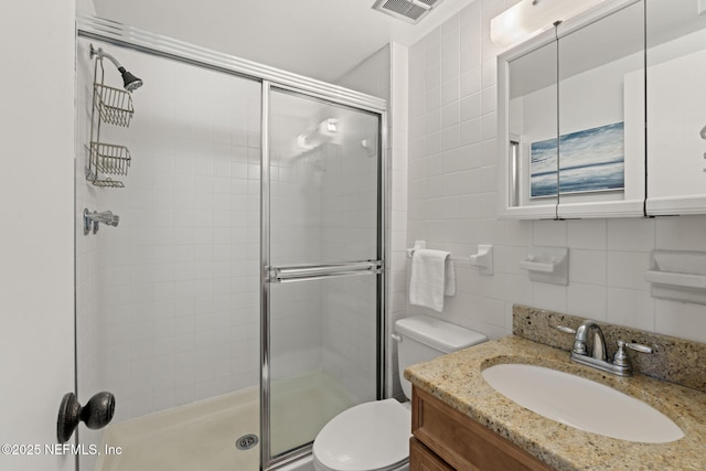 bathroom with vanity, backsplash, toilet, tile walls, and a shower with shower door