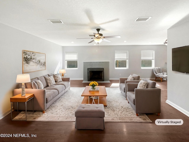 living room with dark wood-type flooring, a fireplace, a textured ceiling, and ceiling fan