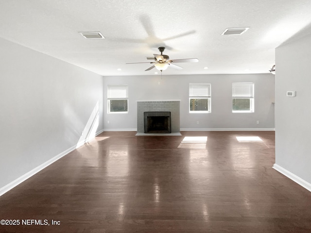 unfurnished living room with dark wood-style floors, a fireplace with flush hearth, visible vents, and a ceiling fan