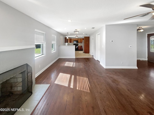 unfurnished living room featuring ceiling fan, a fireplace, baseboards, and wood finished floors