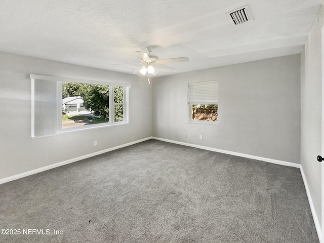 carpeted spare room with baseboards, a textured ceiling, visible vents, and a healthy amount of sunlight