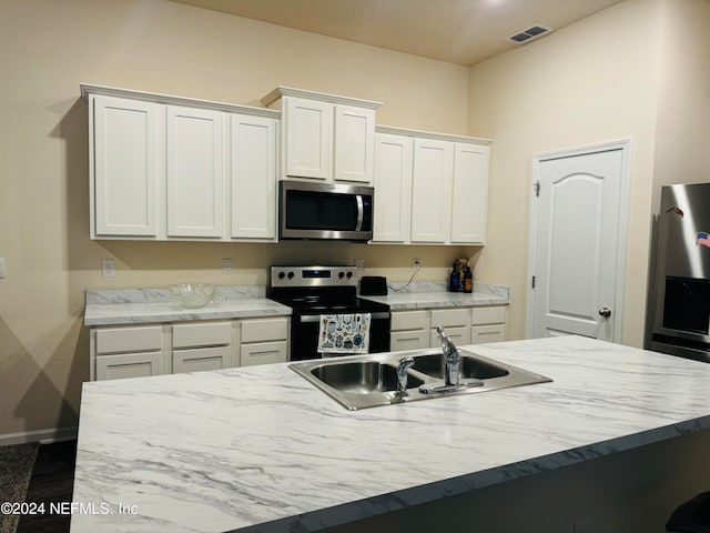 kitchen with white cabinets, stainless steel appliances, a center island with sink, and sink