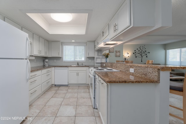 kitchen with white appliances, a tray ceiling, a kitchen bar, kitchen peninsula, and white cabinets