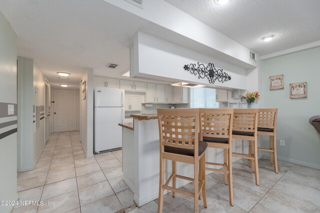 kitchen with white fridge, a textured ceiling, light tile patterned floors, kitchen peninsula, and white cabinets