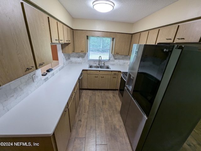 kitchen featuring sink, a textured ceiling, hardwood / wood-style flooring, appliances with stainless steel finishes, and decorative backsplash