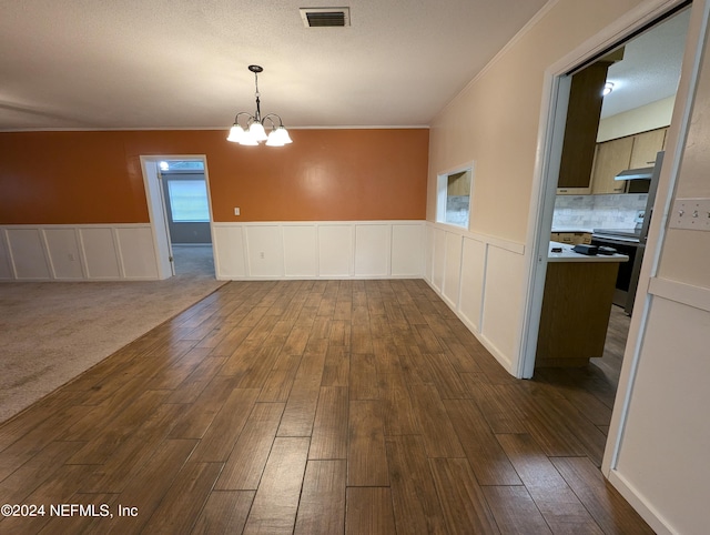 spare room featuring an inviting chandelier, a wealth of natural light, dark wood-type flooring, and crown molding