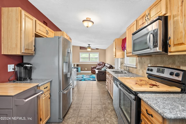 kitchen with vaulted ceiling, light tile patterned floors, stainless steel appliances, sink, and ceiling fan