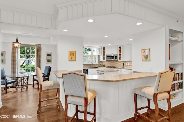 kitchen with hardwood / wood-style flooring, a breakfast bar, kitchen peninsula, and white cabinetry