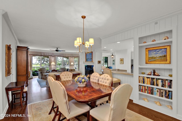 dining area with built in shelves, ceiling fan with notable chandelier, crown molding, and light hardwood / wood-style floors