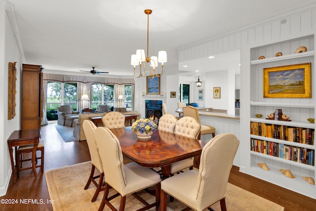 dining room featuring ceiling fan with notable chandelier, built in shelves, hardwood / wood-style flooring, and crown molding