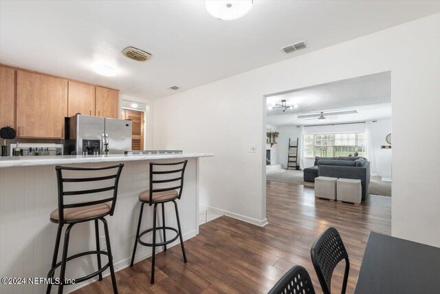 kitchen with a breakfast bar area, stainless steel fridge, dark wood-type flooring, kitchen peninsula, and ceiling fan