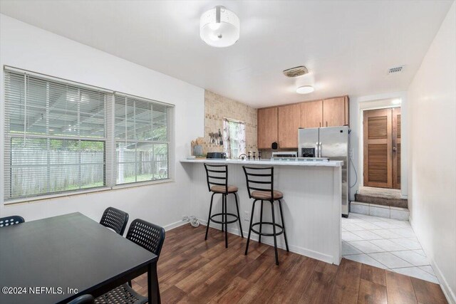 kitchen featuring a kitchen bar, hardwood / wood-style flooring, stainless steel fridge with ice dispenser, and kitchen peninsula