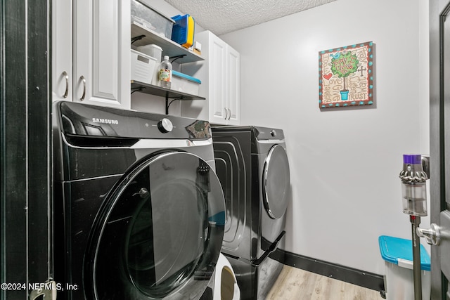 washroom featuring washing machine and clothes dryer, light wood-type flooring, a textured ceiling, and cabinets