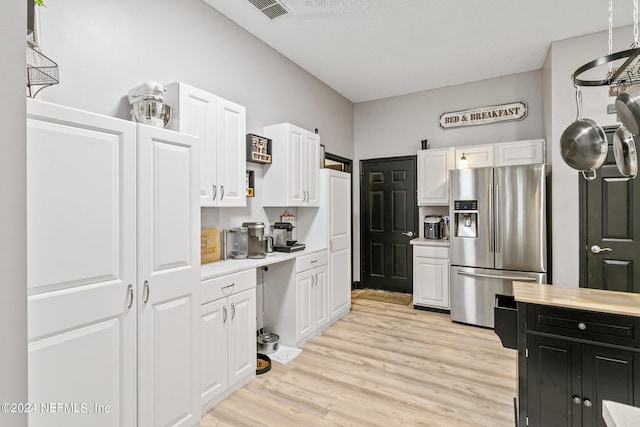 kitchen featuring light wood-type flooring, stainless steel refrigerator with ice dispenser, a textured ceiling, and white cabinets